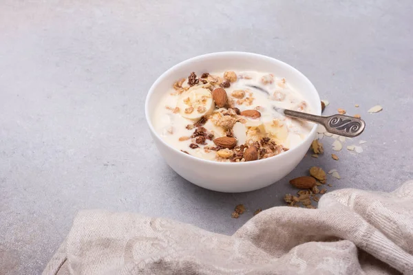 Sağlıklı kahvaltı için yoğurtlu granola, taze muz ve badem fıstığı gri beton arka planda.