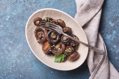 Baharatlı ve maydanozlu ızgara şampiyon mantarları mavi beton arka planda.