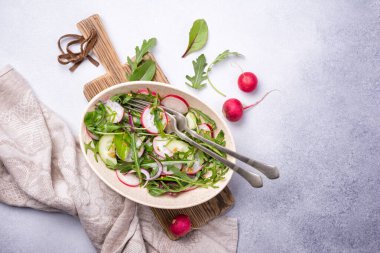 Sağlıklı ve lezzetli vejetaryen yemekleri. Turp, salatalık, soğan, taze yeşil yapraklar ve hardal soslu gri çimento arkaplanlı hafif salata.