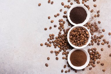 Fotokopi alanı olan gri beton arka planda, beyaz kâselerde öğütülmüş kahve ile kavrulmuş fasulye manzarası.
