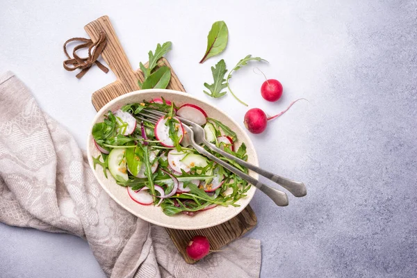 Sağlıklı ve lezzetli vejetaryen yemekleri. Turp, salatalık, soğan, taze yeşil yapraklar ve hardal soslu gri çimento arkaplanlı hafif salata.