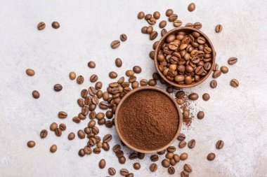 Kavrulmuş fasulye ve açık gri arka planda fincanlarda öğütülmüş kahve.