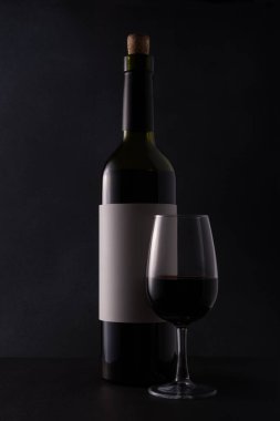 Bottle of red wine with white template or mock-up label and glass on black background