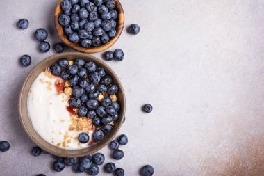 Top view with bowl of healthy dessert or breakfast with yogurt, blueberries and granola on grey concrete background