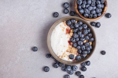 Top view with bowl of healthy dessert or breakfast with yogurt, blueberries and granola on grey concrete background