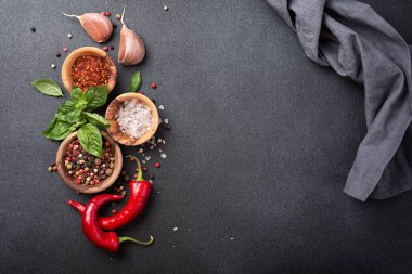 Biberli, tuzlu, sarımsaklı, fesleğenli ve kırmızı acı biberli baharatlı ve aromalı yiyeceklerden oluşan koyu beton arka planda fotokopi alanı olan üst manzara.