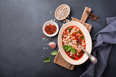 Baharatlı, domates soslu fasulye ve koyu beton arka planda taze fesleğen.