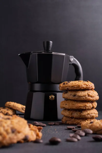 Homemade tasty chocolate chip cookies with black geyser coffee maker on dark concrete background