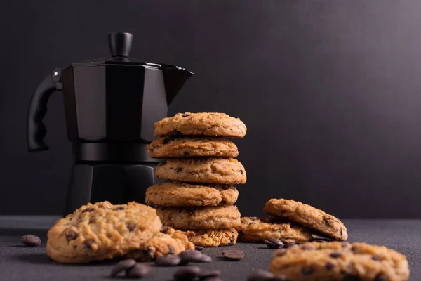 Homemade tasty chocolate chip cookies with black geyser coffee maker on dark concrete background