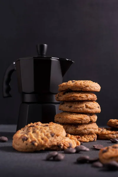 Homemade tasty chocolate chip cookies with black geyser coffee maker on dark concrete background