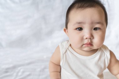 Yatak odasındaki beyaz yatakta oturan şirin bebek portresi. Metin için seçici odak alanı. Pankart tasarımı