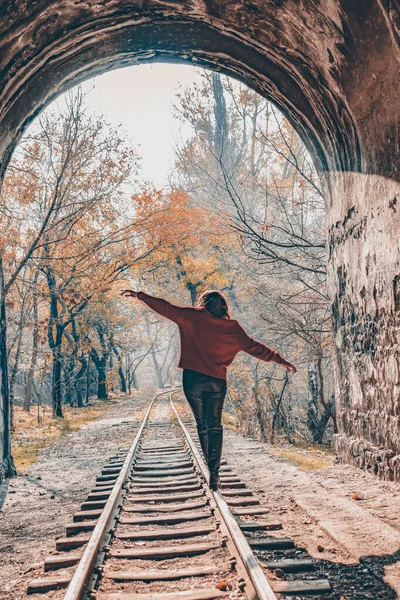 Kız tünelden geçen demiryolunda yürüyor. Tünel doğruca ormana çıkıyor.
