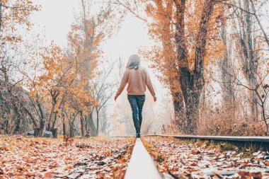 Kadın, demiryolu ve peri ormanı. Güzel bir kadın sonbahar ormanında demiryolunda yürüyor.