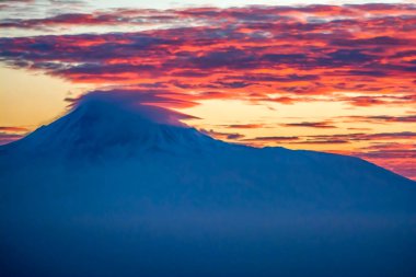 The top of the mountain is covered with clouds. Red clouds at the peak of the mountain during sunset. Beautiful sunset