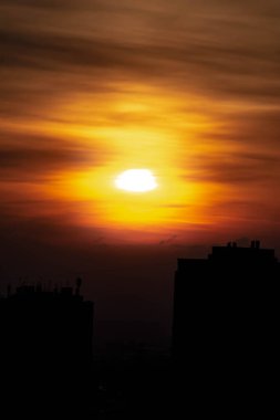 Gökdelenlerin üzerinde gün batımı. Büyük şehir evleri ve turuncu gökyüzü parlak güneş.
