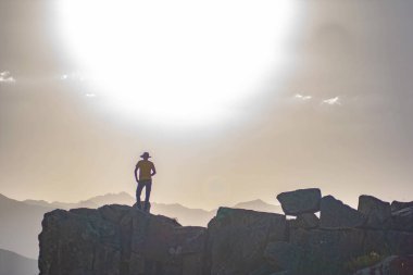 The man is standing on a rock. Man against the backdrop of sunset. Silhouette of a man and the sun