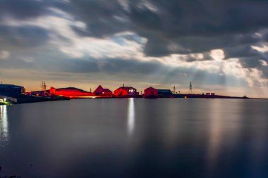 Night sky and shining lake. Night cloudy sky and houses next to the lake. Reflection of the moon on the lake. Scenic view