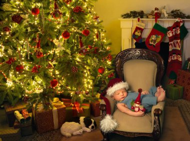 Noel Baba şapkalı yeni doğmuş bebek Noel ağacının yanındaki koltukta uyuyor.