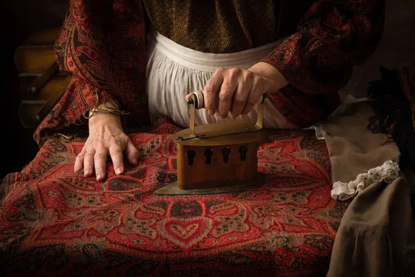 穿着维多利亚式衣服的老妇人在木板上用古老的炭铁干活 — 图库照片