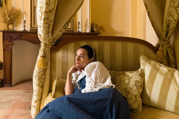 Ortaçağ Fransız şatosunun altın yatak odasındaki lüks bir antika tepe örtüsünün üzerinde duran otantik rönesans kostümü giymiş güzel bir kadının Hollanda Ustası tarzı portresi.