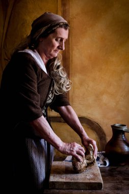 Woman in authentic peasant renaissance costume breaking the bread.