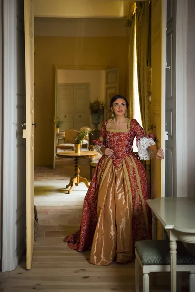 Beautiful woman in late renaissance costume posing between the open doors of a medieval castle.