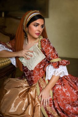 Young woman in medieval renaissance costume and French hood sitting on the floor holding a letter