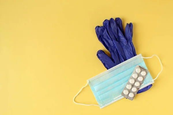Medical mask, blister of tablets and blue medical gloves on yellow background — Foto Stock