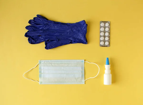 Flat lay of medical mask, nasal spray, blister of tablets and medical gloves on yellow background — Foto Stock