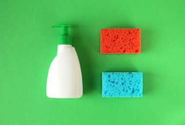 Yeşil arka planda düz bir bulaşık deterjanı ve süngerler.