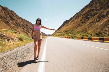 a young single woman of easy virtue, in light sexy clothes, voting on a highway in the desert, traveling alone