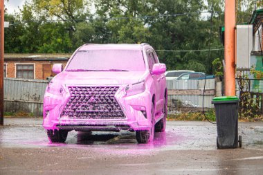 a car treated with pink washing foam at a self-service car wash on the outskirts of the city