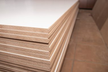 Bir dolap dükkanında düzgünce istiflenmiş bir yığın MDF paneli, arka plan bokeh efektiyle bulanıklaştırılmış