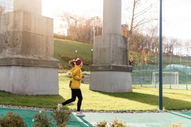 Sonbahar parkında üst geçidin altında koşan genç bir kadın.
