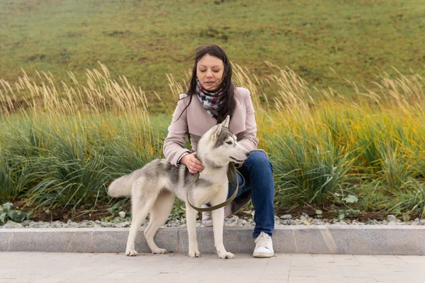 公園の秋草に対して若い女性が犬とコミュニケーションを取り — ストック写真