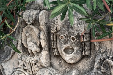 fragment of a wall with stone-cut mask among vegetation in the ruins of the ancient city of Mira, Turkey