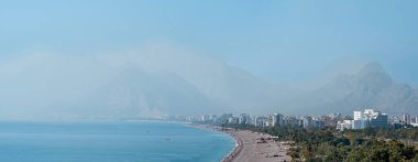 Antalya, Türkiye - 15 Kasım 2021: yakınlardaki kayalıklardan Konyaalti plajının manzarası. Arka planda sisli Beydaglari dağları görülüyor.