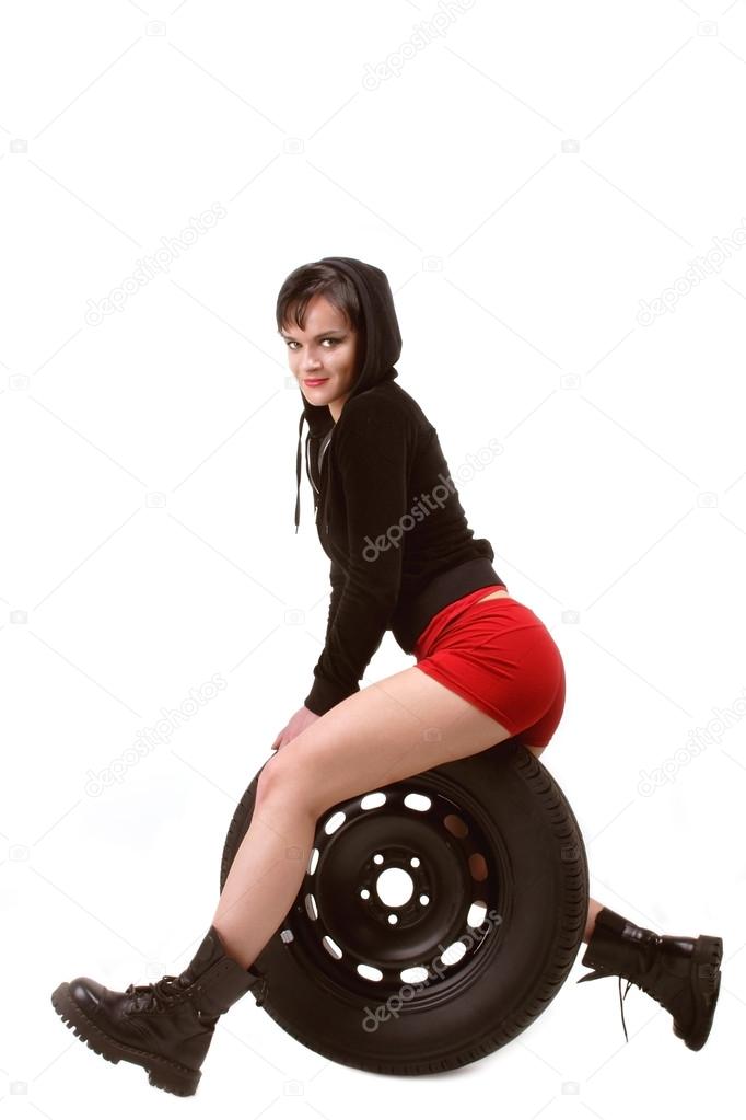 Smiling brunette girl in red shorts and leather boots sitting on car tire