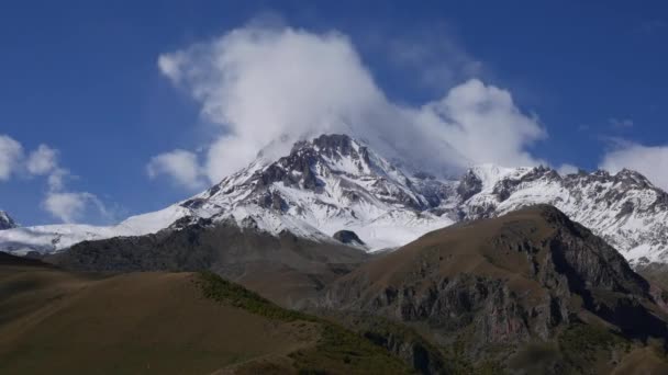 Mount Kazbek or Kazbegi is covered with snow. The wind blows snow from the top of the mountain. Stepantsminda, Georgia. — Stock Video