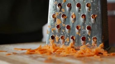 Bir kadının elleri, rende üzerinde havuç ızgara yapar. Ev hanımı mutfakta havuç rendeliyor..