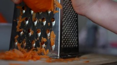 Bir kadının elleri, rende üzerinde havuç ızgara yapar. Ev hanımı mutfakta havuç rendeliyor..