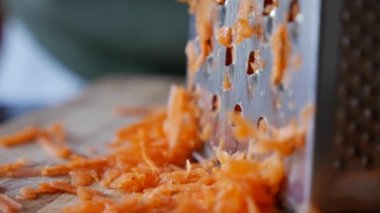 Bir kadının elleri, rende üzerinde havuç ızgara yapar. Ev hanımı mutfakta havuç rendeliyor..