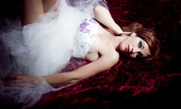 Schöne und sinnliche rothaarige Frau, die auf einem Rosenbett liegt — Stockfoto