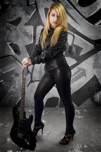 Сексуальна молода блондинка одягнена в чорну шкіру з електрогітарою — стокове фото