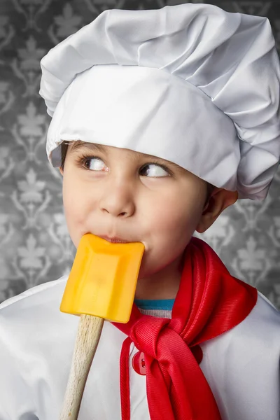 A little boy cook in uniform over vintage background playing wi — Stock Photo, Image