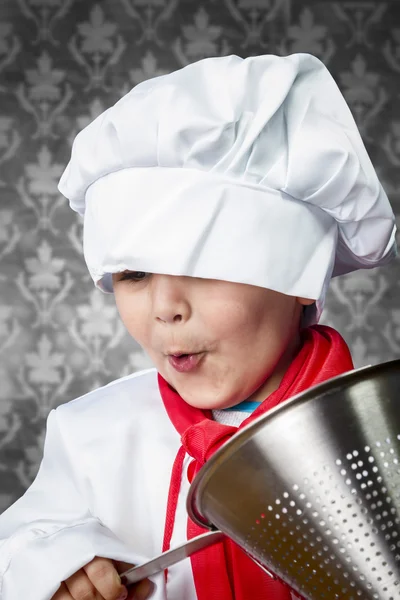 Funny boy cook in uniform over vintage background playing with — Stock Photo, Image