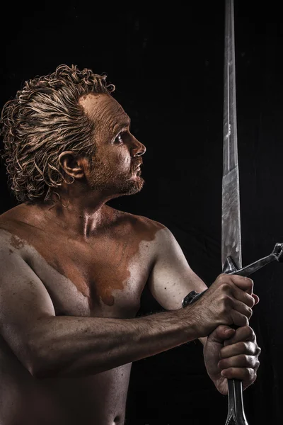 Strong warrior licking a big sword, covered in mud and naked — Stock Photo, Image