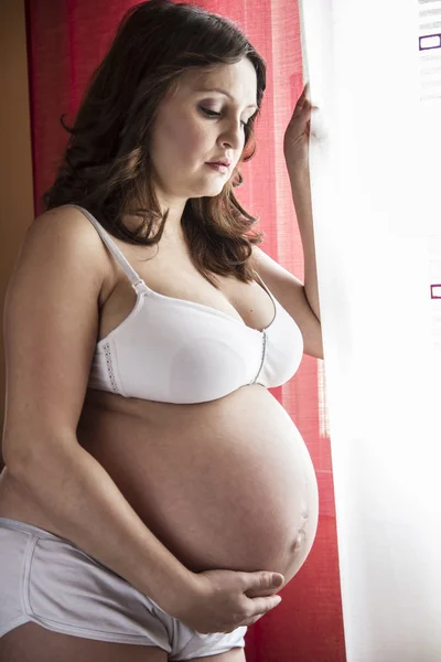 Donna incinta guarda fuori dalla finestra — Foto Stock