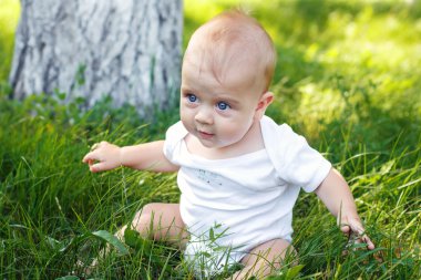 Küçük çocuk çimenlerde oturuyor.
