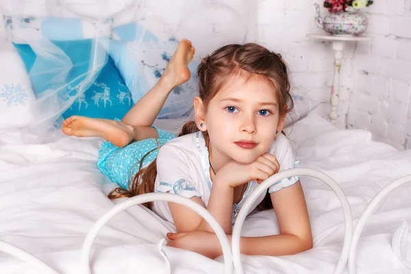 Menina bonita senta-se no cobertor branco em seu quarto — Fotografia de Stock